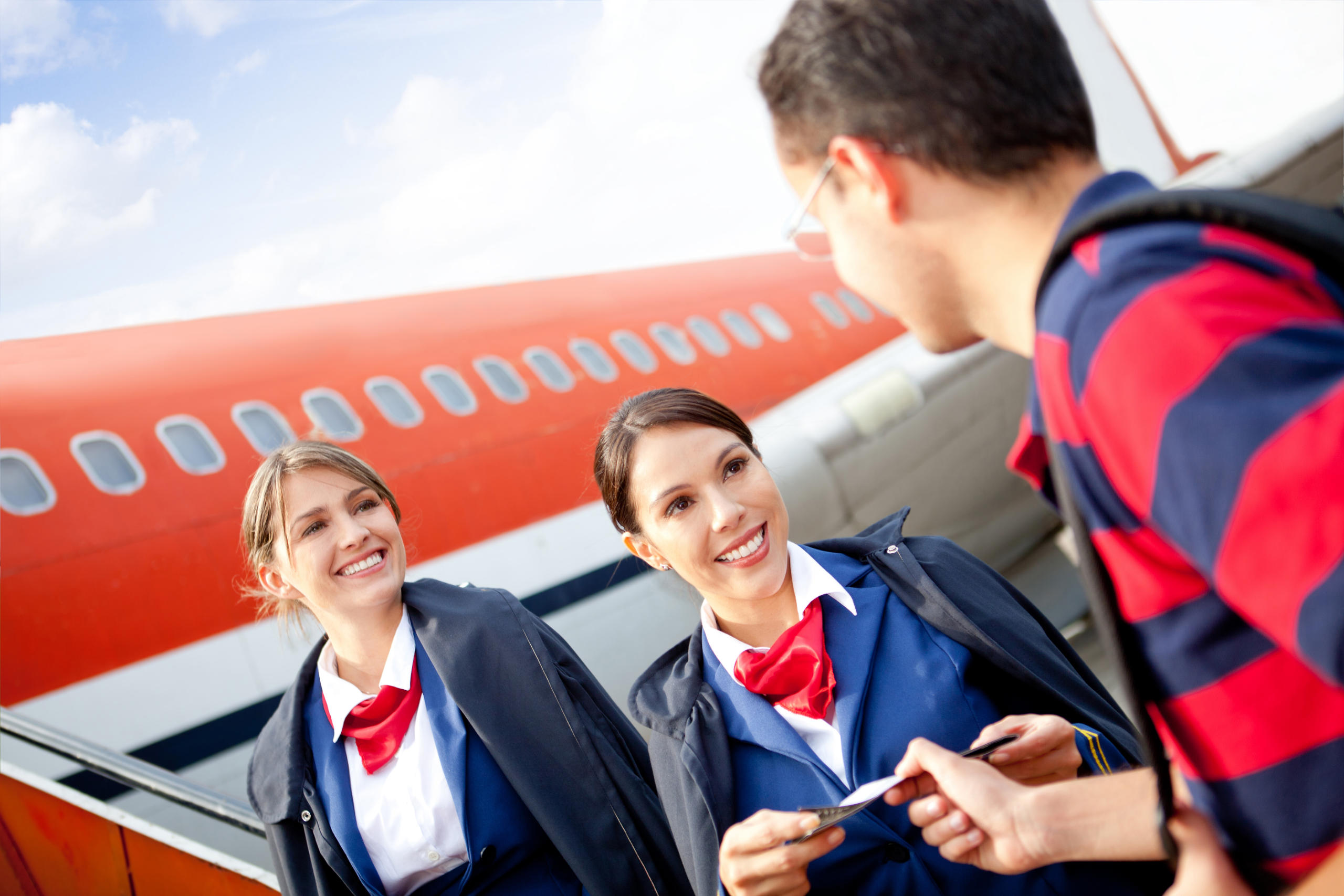 Friendly Flight Attendants Welcoming Passenger Into The Airplane